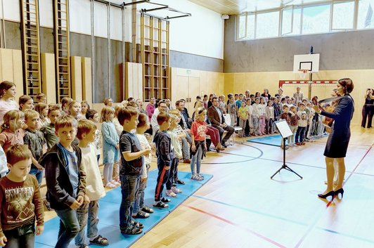 Die Kinder der Volksschule Stainach-Pürgg stehen im Turnsaal und singen mit den Lehrern ein Lied