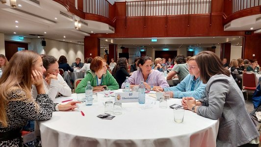 In einem Konferenzraum sitzen mehrere Personen an einem runden Tisch und sprechen miteinander