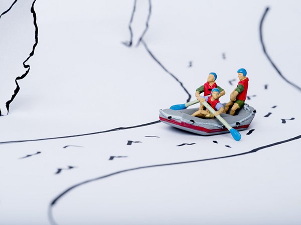 Drei Spielzeigfiguren sitzen in einem Spielzeugboot und fahren auf einem gezeichneten Fluss
