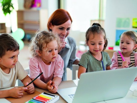 Kindergärtnerin mit Kindern vorm Laptop