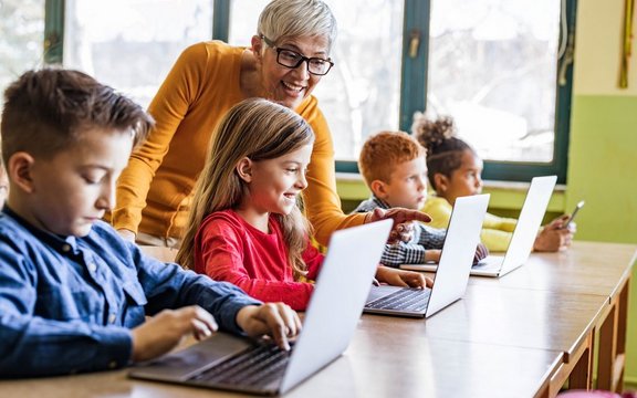 Lehrerin, die ihren Schüler/innen hilft, Laptops in der Klasse zu benutzen.