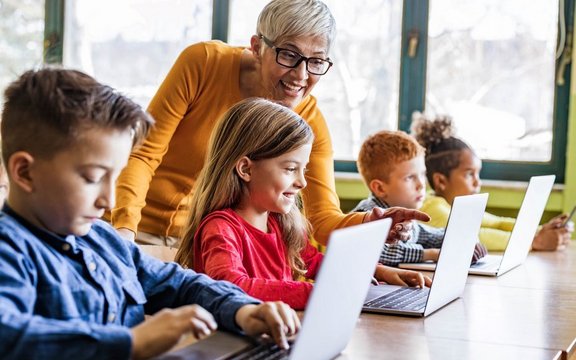 Lehrerin, die ihren Schüler/innen hilft, Laptops in der Klasse zu benutzen.