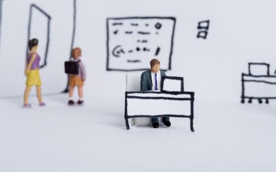 Spielfiguren sind in einem gezeichneten Klassenzimmer. Lehrer sitzt auf einer Schulbank vor dem Computer