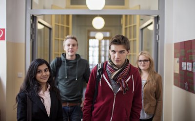 Vier Schüler und Schülerinnen gehen in einem Schulgang der Kamera entgegen